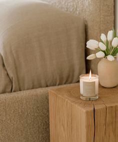 a white candle sitting on top of a wooden table next to a vase with flowers