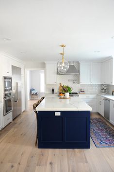 a large kitchen with white cabinets and blue island in front of the stove top oven