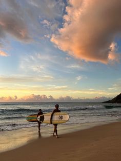 two surfers walking on the beach with their surfboards under an orange and blue sky