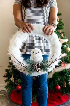 a woman standing in front of a christmas tree holding an owl wreath with pine cones on it