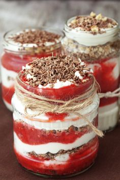 three jars filled with desserts sitting on top of a wooden table next to a spoon