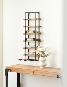 a wooden table topped with two wine glasses and a vase filled with flowers next to a wall mounted wine rack