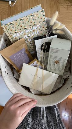 a basket filled with lots of different items on top of a wooden floor next to a person's hand