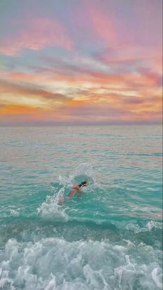 a person swimming in the ocean under a colorful sky at sunset or sunrise with clouds