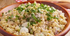 a wooden bowl filled with macaroni salad on top of a table next to a red and white checkered napkin