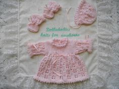 a pink knitted baby outfit and booties on top of a white doily