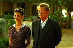 an older man and young woman standing next to each other in front of a house