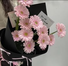 a bouquet of pink flowers sitting on top of a black box with a note attached to it