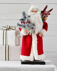 a santa clause figurine holding a christmas tree next to presents on a table