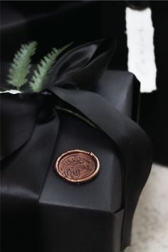 a black gift box with a wax stamp on it and a fern in the corner