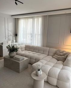 a large white sectional couch in a living room with two vases on the end tables