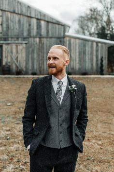 a man wearing a suit and tie standing in front of a barn