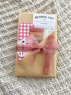 an open book with pink ribbon on it sitting on top of a white knitted blanket