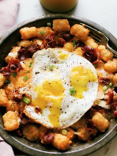 an egg is on top of tater tots in a skillet