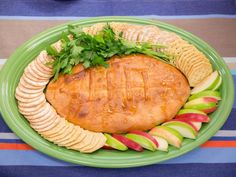 a green plate topped with fruit and crackers on top of a blue table cloth