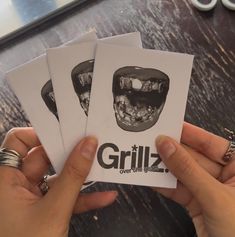 two hands holding up three cards with the words grillz on one side and an image of a man's mouth