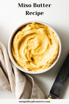 a white bowl filled with hummus next to a knife on top of a table