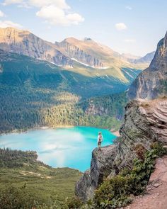 a person standing on the edge of a cliff overlooking a mountain lake and mountains in the distance