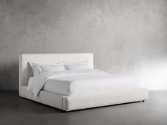 a bed with white linens and pillows in a room that looks like it has concrete walls