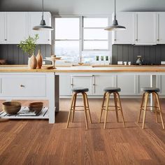 a kitchen with white cabinets and wooden floors, two stools in front of the island