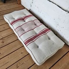 a white and red striped bench cushion sitting on a wooden floor next to a brick wall