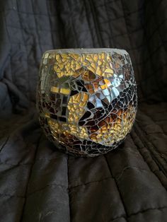 a mosaic glass candle holder sitting on top of a black cloth covered bed spreader