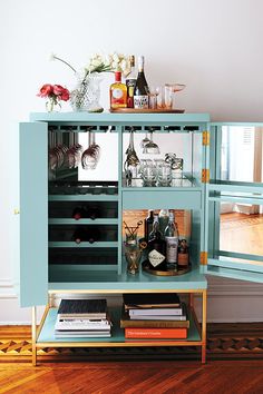 a blue cabinet filled with bottles and glasses on top of a hard wood floor next to a wall