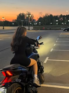 a woman riding on the back of a motorcycle down a street at sunset or dawn