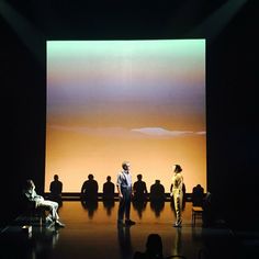 several people sitting on chairs in front of a large screen with an orange sky behind them