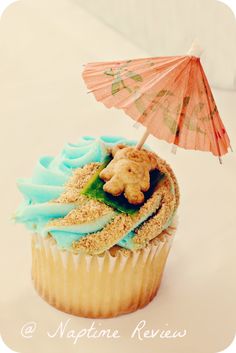 a cupcake with blue frosting, an umbrella and a teddy bear on top