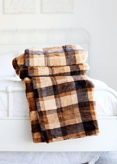 a bed with a plaid blanket on top of it next to a white headboard