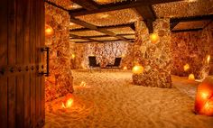 an indoor spa with candles lit on the floor and stone walls, surrounded by sand