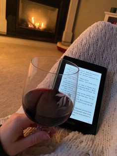 a person is holding a glass of wine and looking at the screen on their tablet