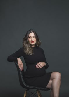 a woman sitting on top of a chair in front of a gray background with her legs crossed