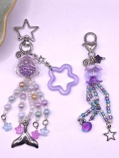 two key chains with charms on them sitting next to each other, one has a star and the other is a mermaid