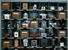 an assortment of old cameras on display in a metal shelf with wooden crates and bins