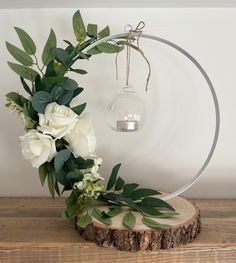 white flowers and greenery are arranged in front of a circular light fixture on a wooden table