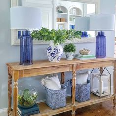 a wooden table topped with blue vases filled with flowers and greenery next to a mirror