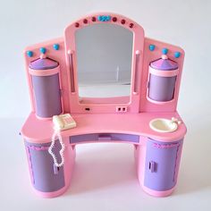 a pink and purple toy desk with a mirror on it's top, phone plugged in