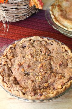 a pie sitting on top of a wooden table next to a basket filled with leaves