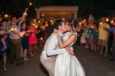 a bride and groom kissing while surrounded by people holding sparklers