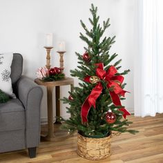 a small christmas tree with red bows in a basket next to a couch and table