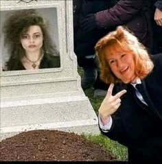 a woman pointing at the camera in front of a grave with a photo on it