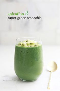 a green smoothie in a glass next to a spoon