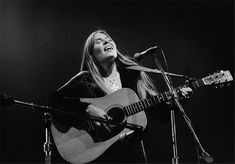 a woman singing into a microphone while holding an acoustic guitar in front of a microphone