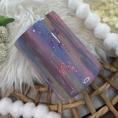 a purple and blue flask case sitting on top of a white fluffy rug next to flowers