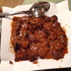 a white plate topped with meat covered in gravy and a spoon next to it