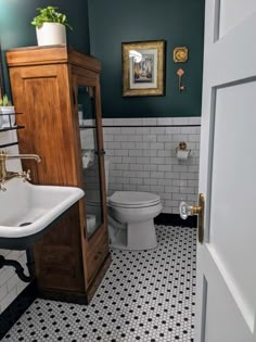 a white toilet sitting next to a wooden cabinet in a bathroom with black and white tiles