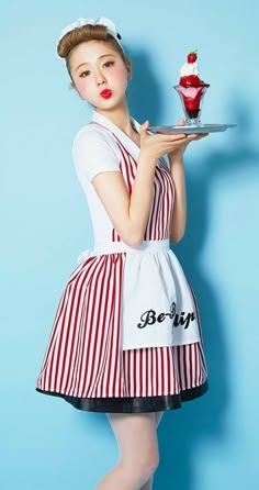 a woman dressed in an apron holding a plate with a cupcake on top of it