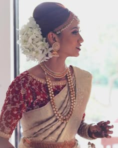 a woman in a red and white sari with flowers on her head, wearing jewelry